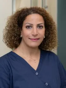 Porträt einer lächelnden Person mit kurzem, lockigem Haar und dunkler Bluse