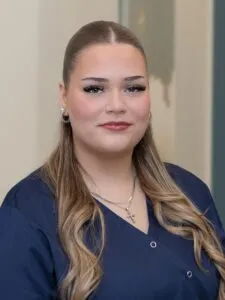Eine Person mit glatt zurückgebundenem Haar und dunklem Oberteil