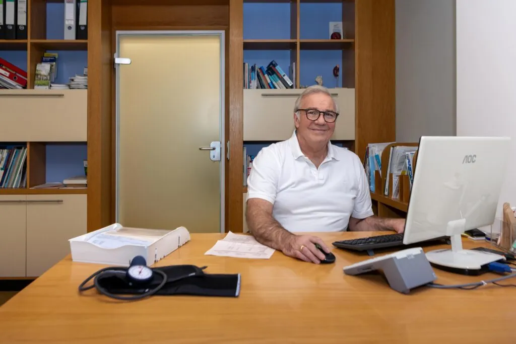 Dr. Georg Mayer sitzt lächelnd an einem Schreibtisch mit Computerausstattung und Büromaterial.