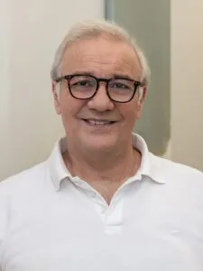 Ein lächelnder älterer Herr mit Brille und weißem Hemd
