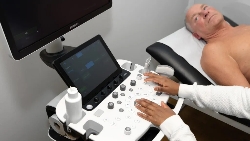 Ein Arzt führt eine Ultraschalluntersuchung an einem liegenden Patienten durch.