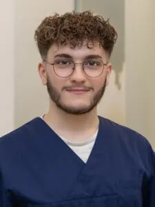 Ein junger Mann mit Brille und kurzem, lockigem Haar, der lächelt