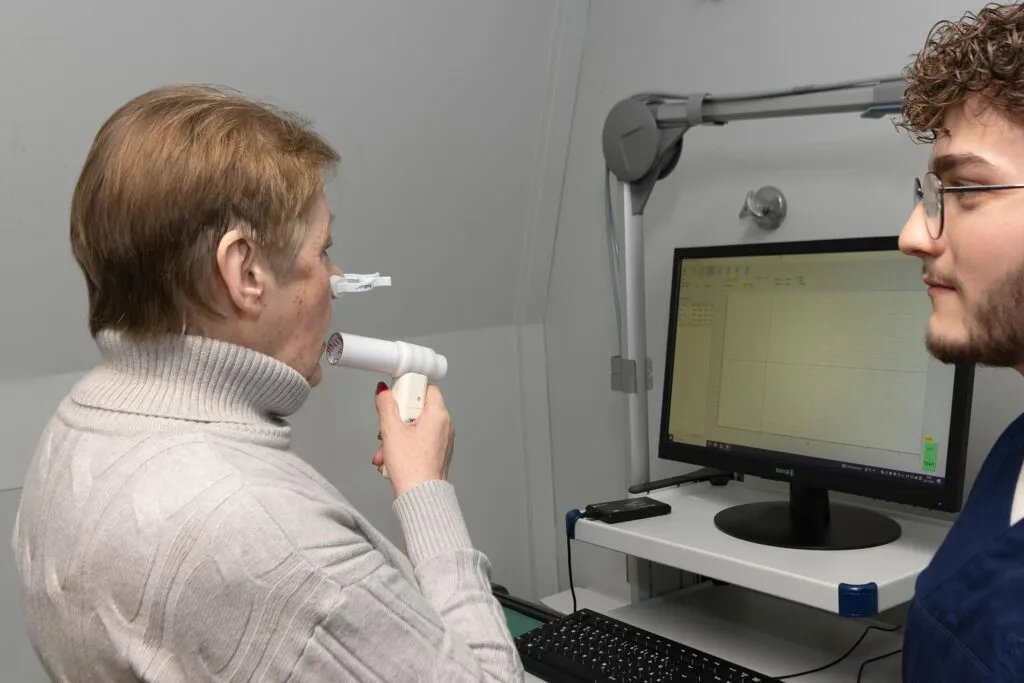 Eine Person führt eine Messung mit einem tragbaren Gerät an der Nase einer anderen Person durch, während eine dritte Person auf einen Computerbildschirm schaut.